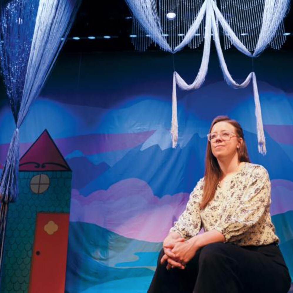 Grace Cannon Wallace sitting in front of a cloth backdrop of a tower and mountains.