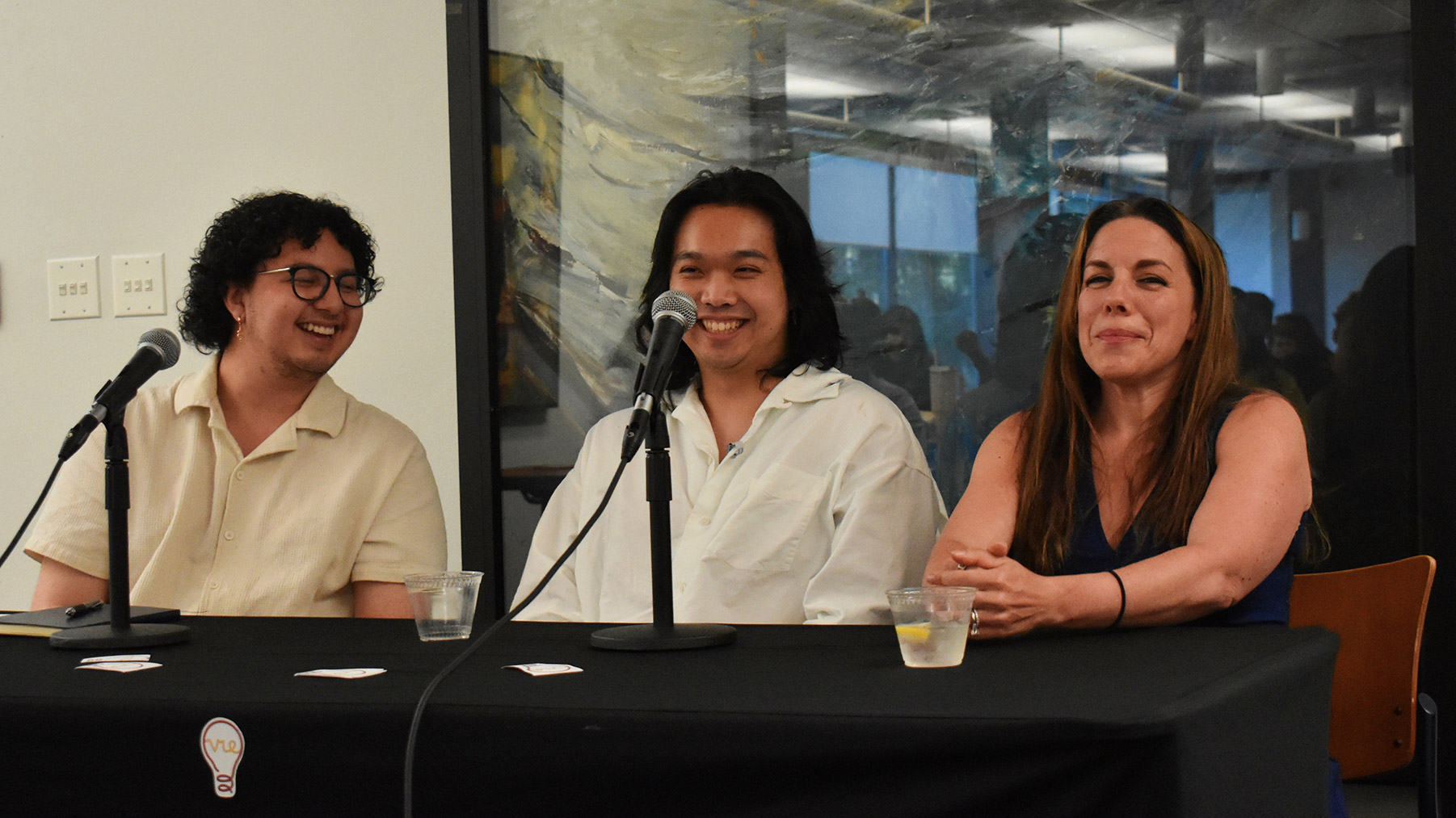 Three people sitting at a table smiling with microphones in front of them