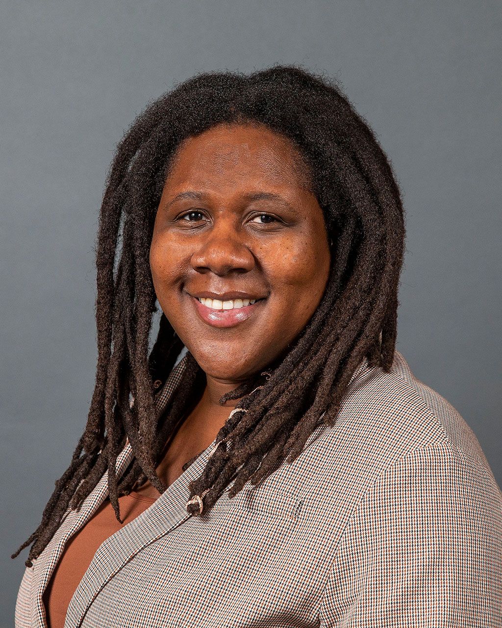 A person with long, dark brown hair call and a gray jacket smiles at the camera