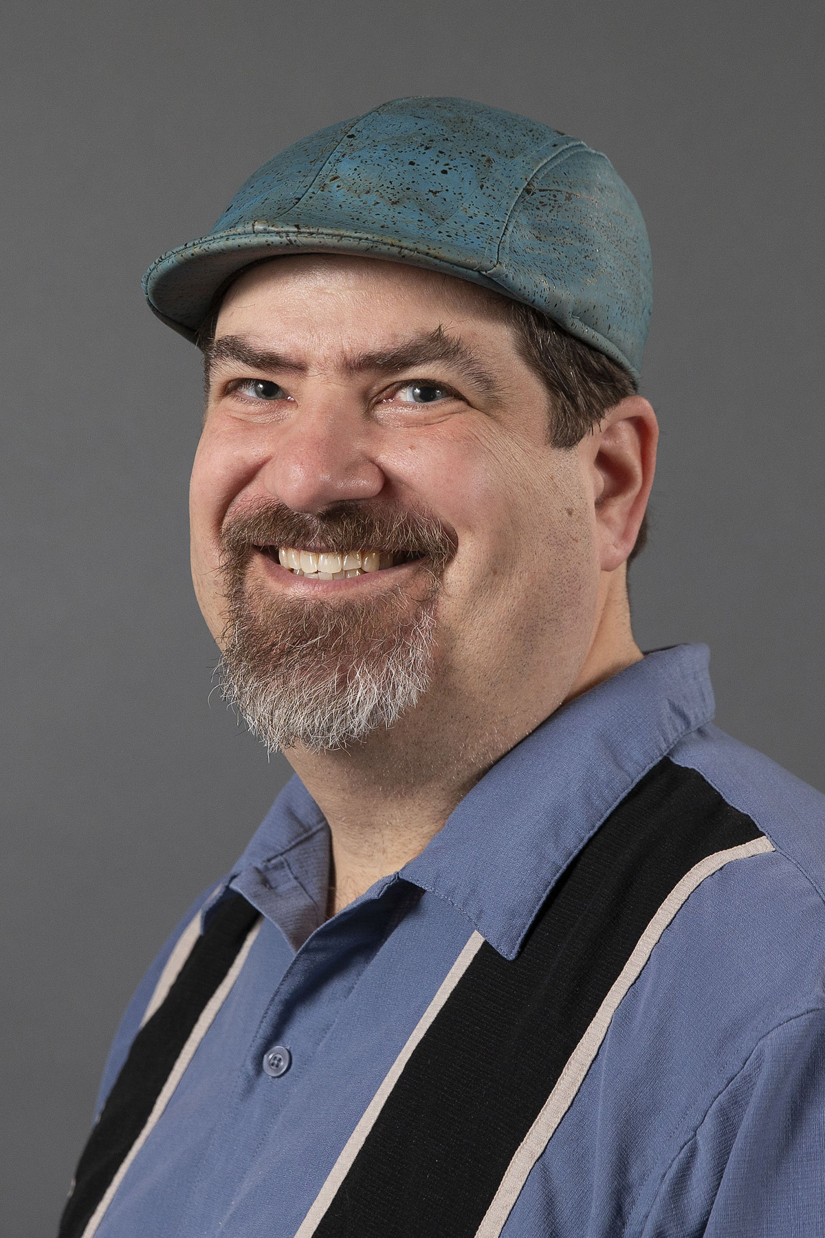 Man in a blue shirt and derby hat smiling