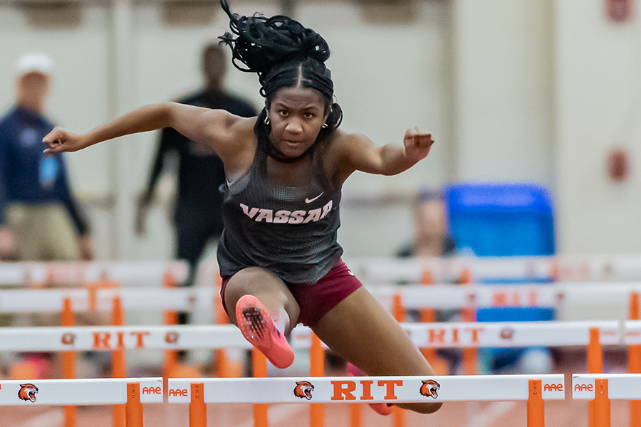 Jahmilia Dennis, with long hair streaming behind, her leaps over a hurdle.