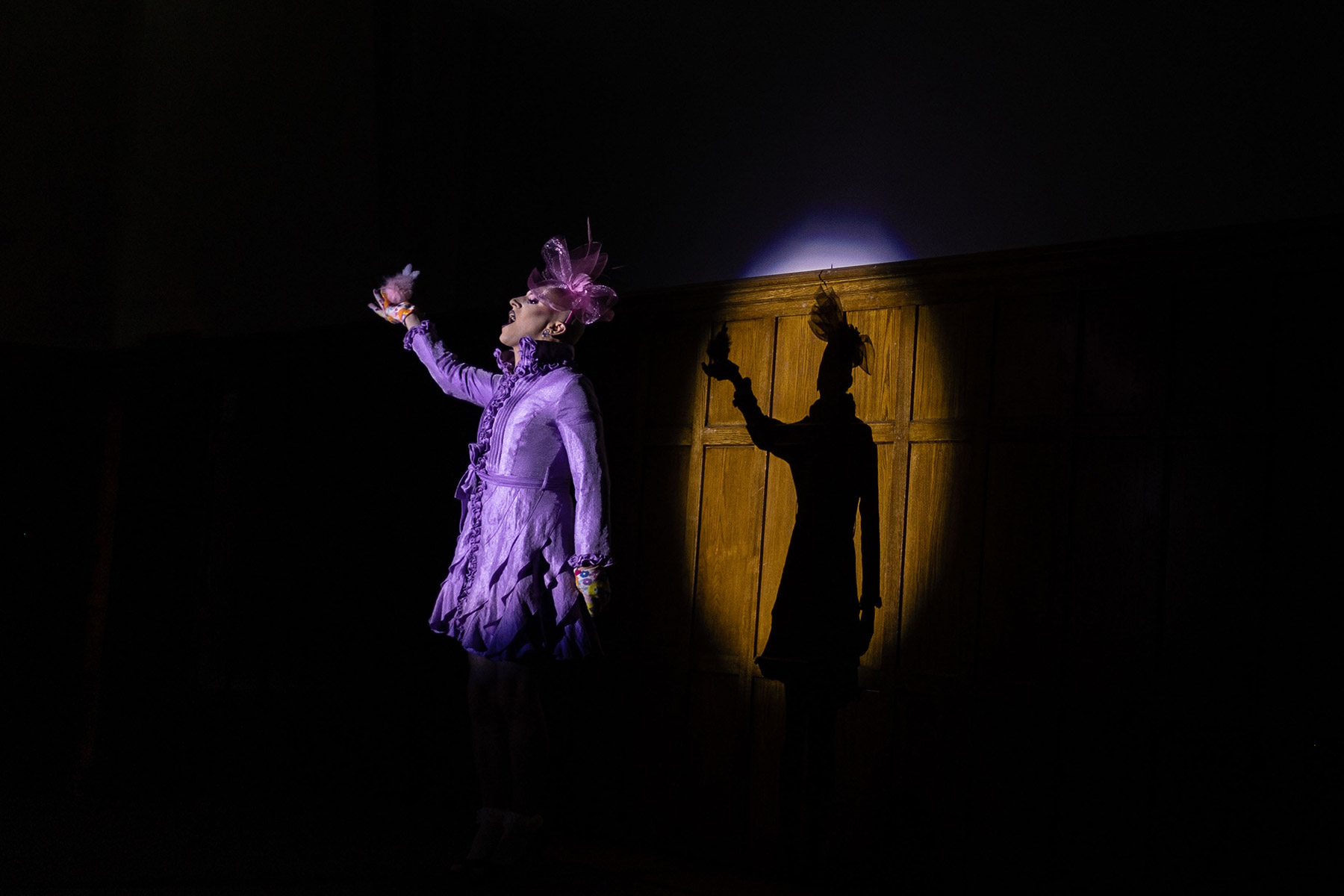 Woman with purple jacket on a dark stage with a spotlight highlighting her.