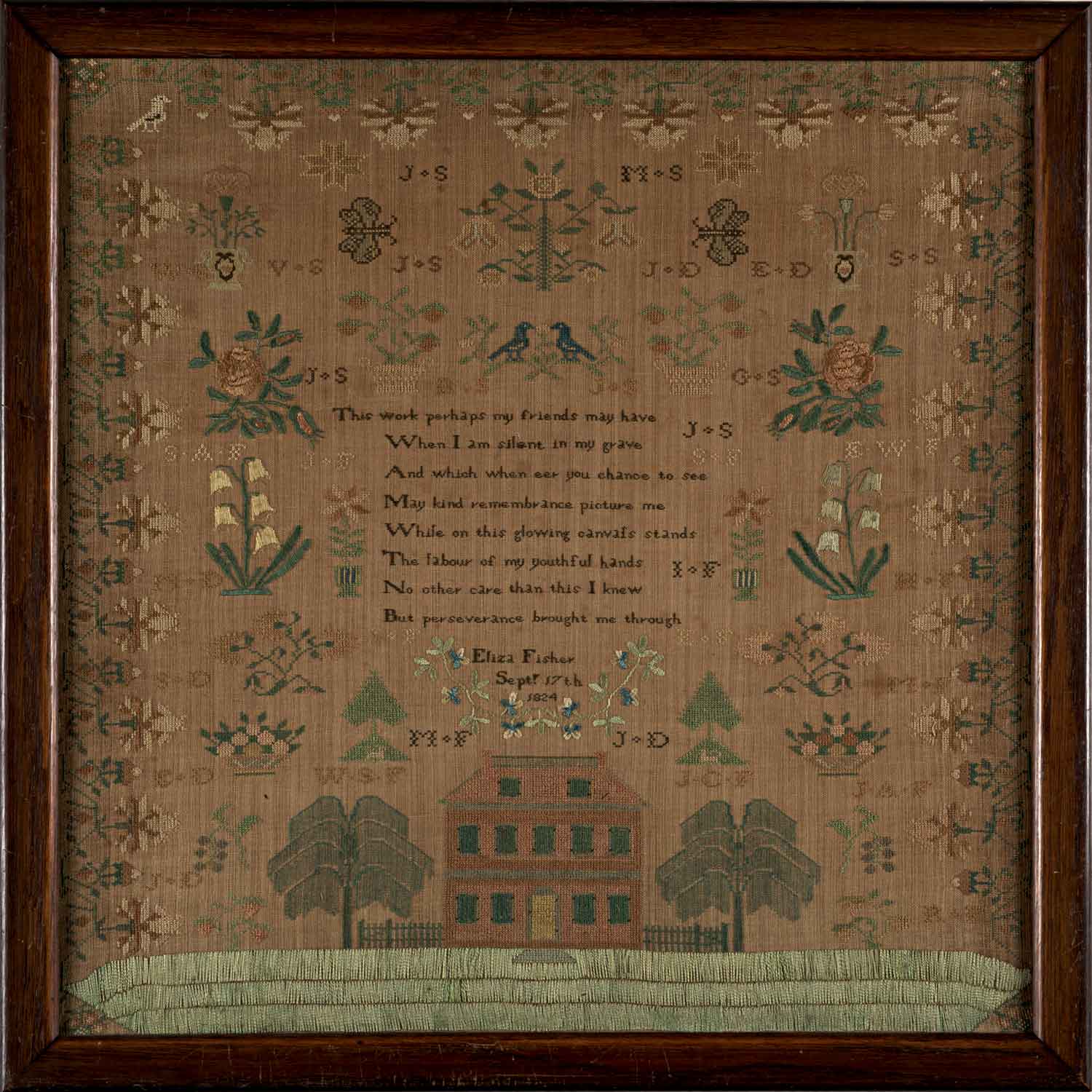 Photo of a needlework with a house and trees under stitched text that is hard to read