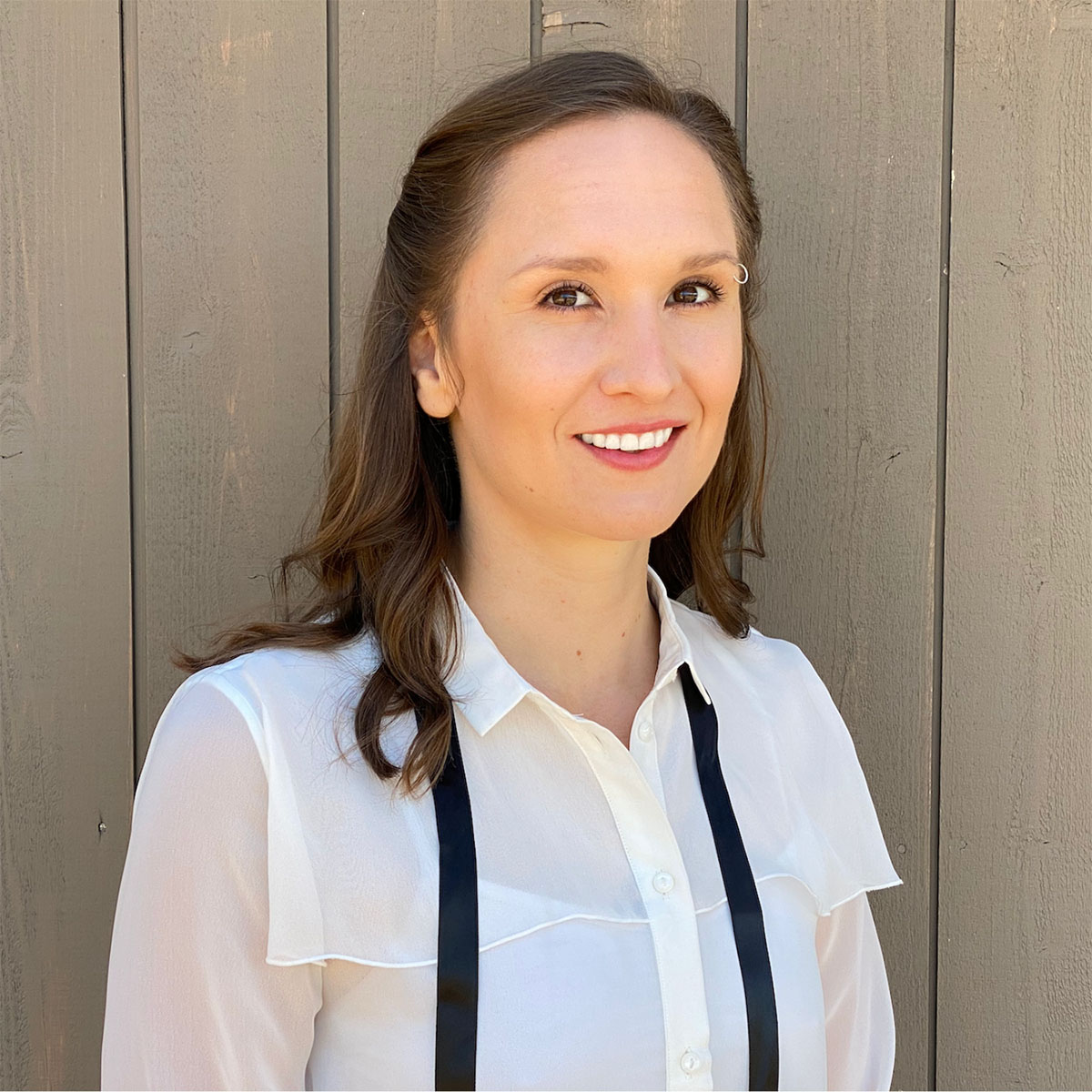Hillary Lyons wearing a white collar shirt standing in front of a wood board building.