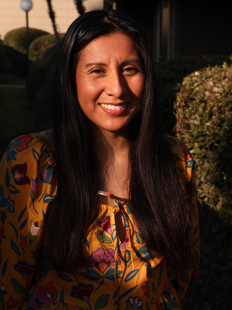 Candy Martinez headshot wearing an orange flower patterned shirt and has long dark hair.