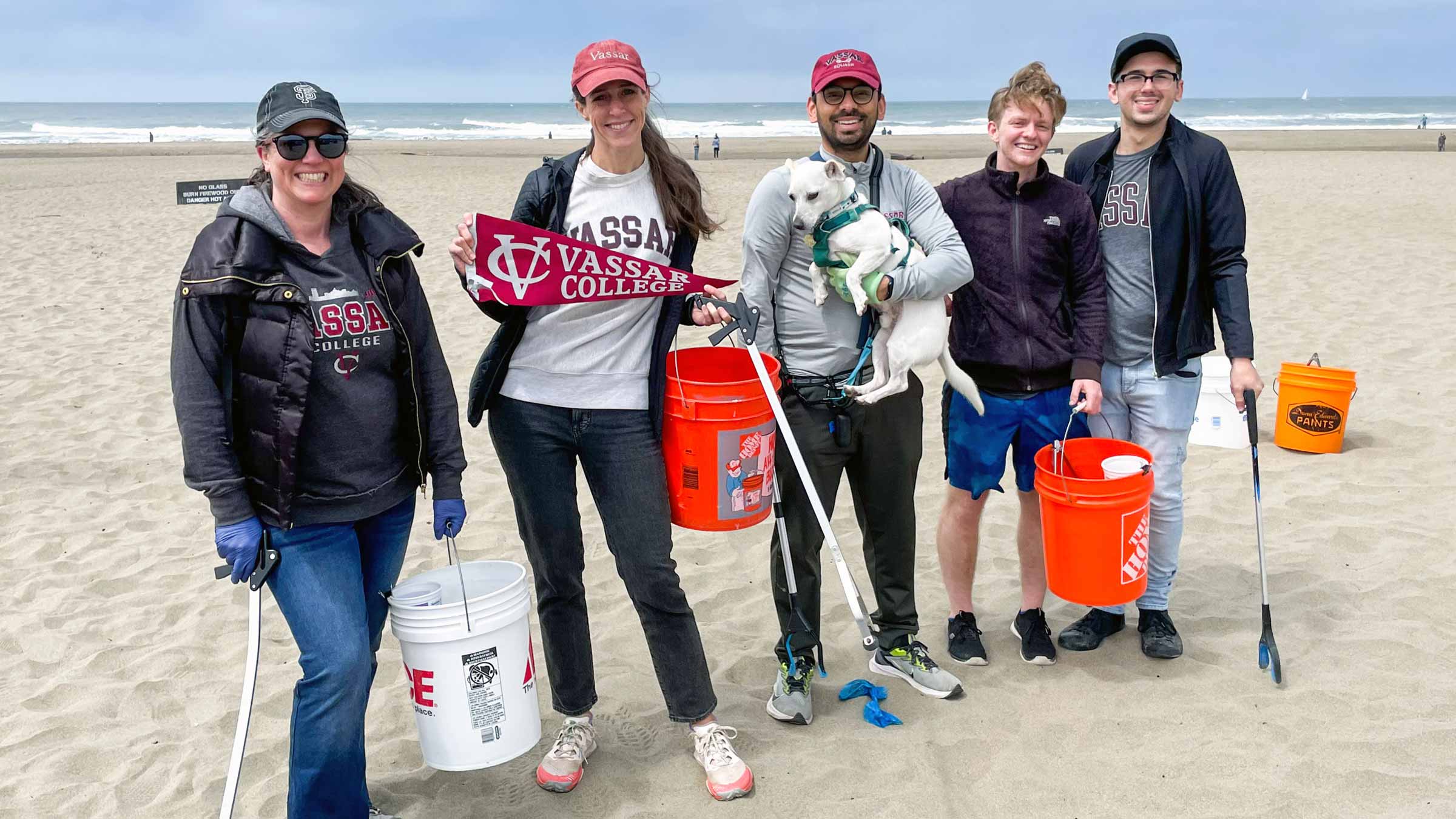 A group of people standing together on a beach holding a Vassar banner