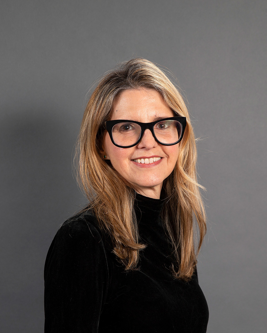 Eva Woods Peiró wearing a black shirt against a gray background.