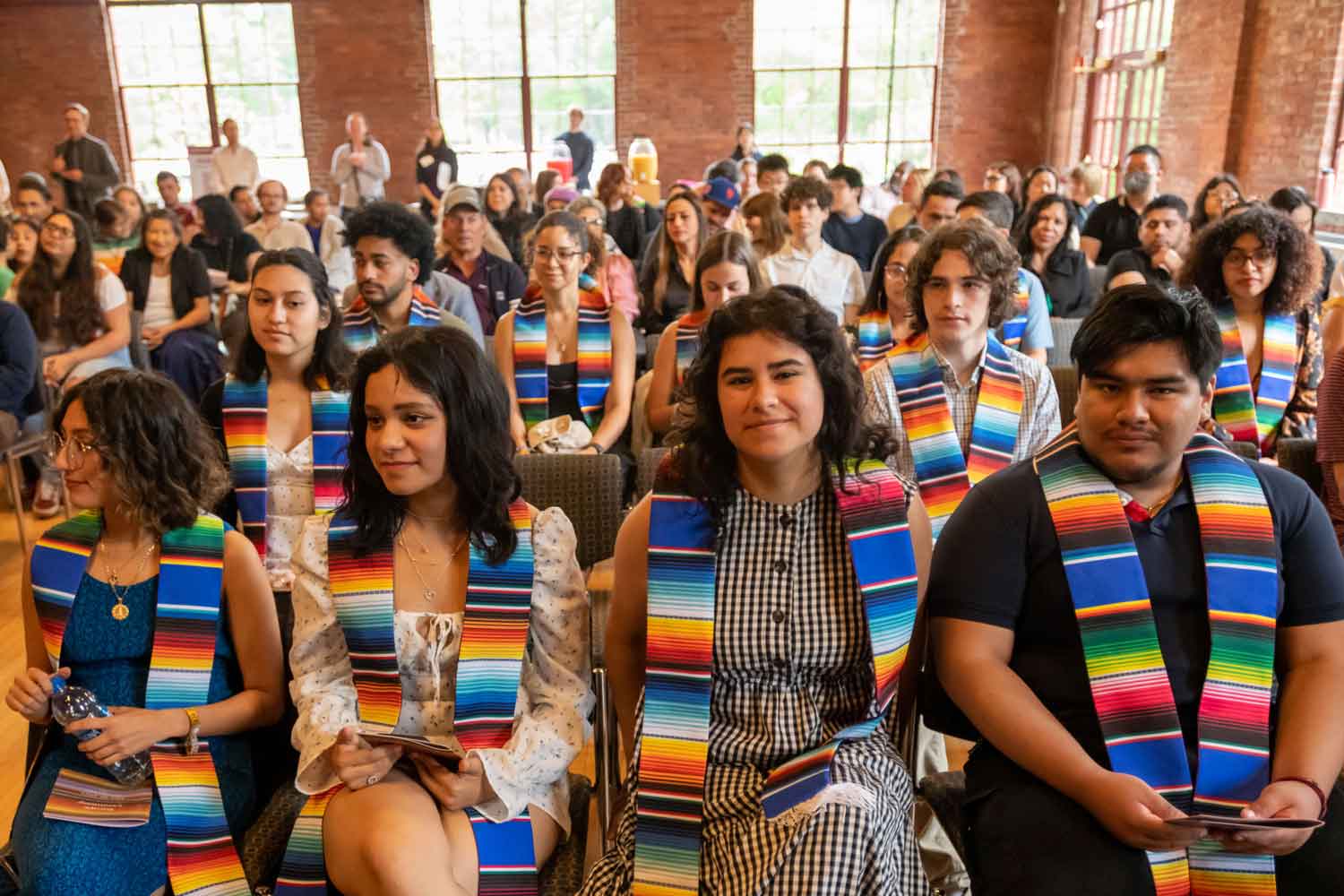seated people at ceremony smiling and wearing multicolored stoles