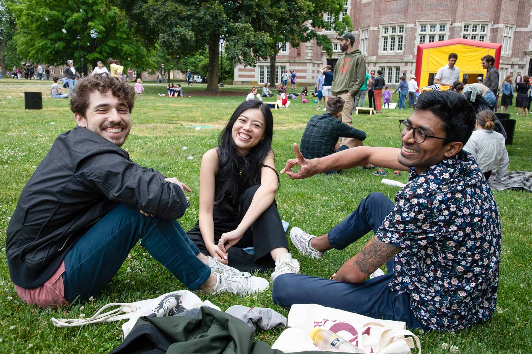 Groups of people sitting on the lawn with a red and yellow bouncy house in the background