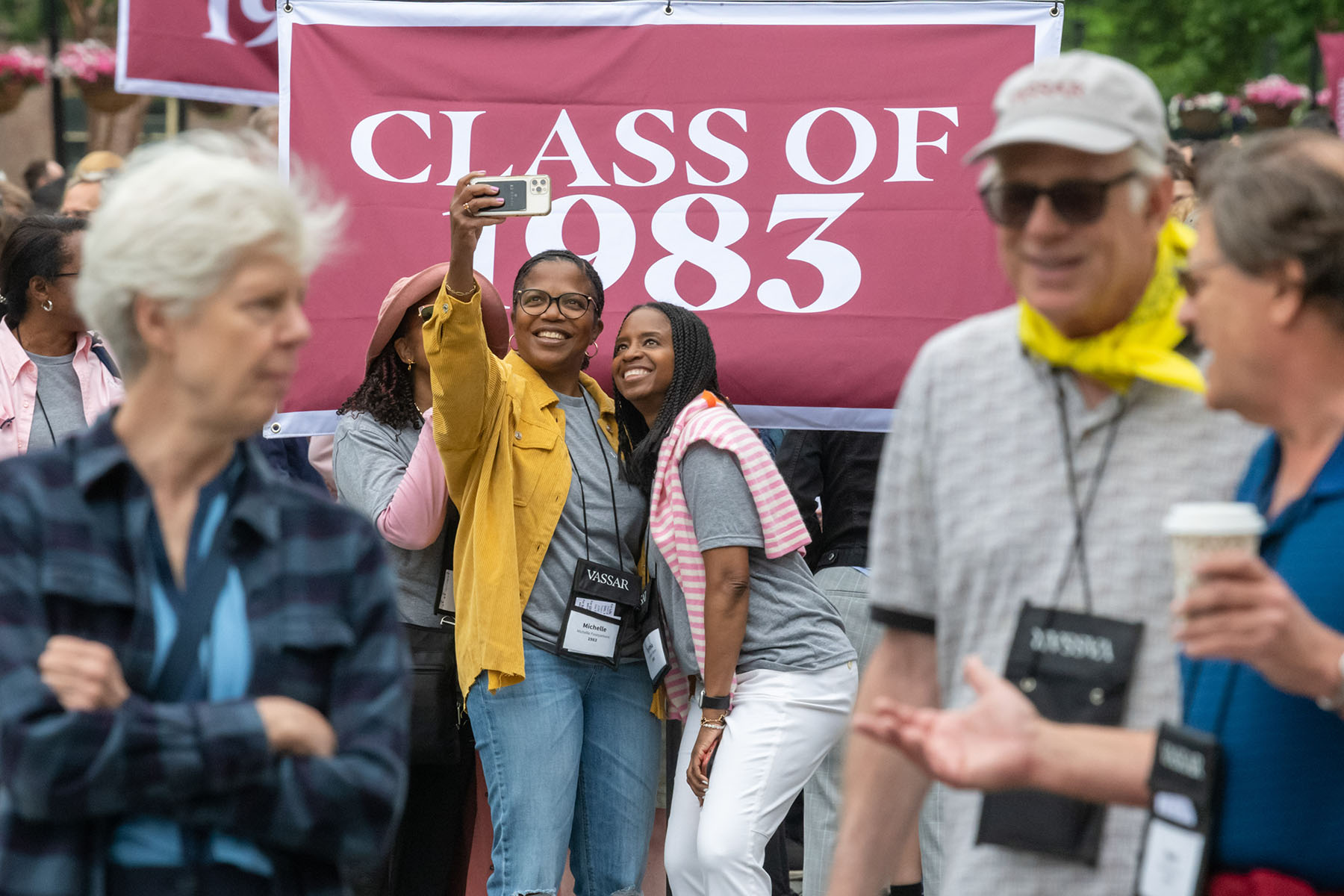 Three women taking a selfie in front of a large burgundy and white banner saying "Class of 1983"