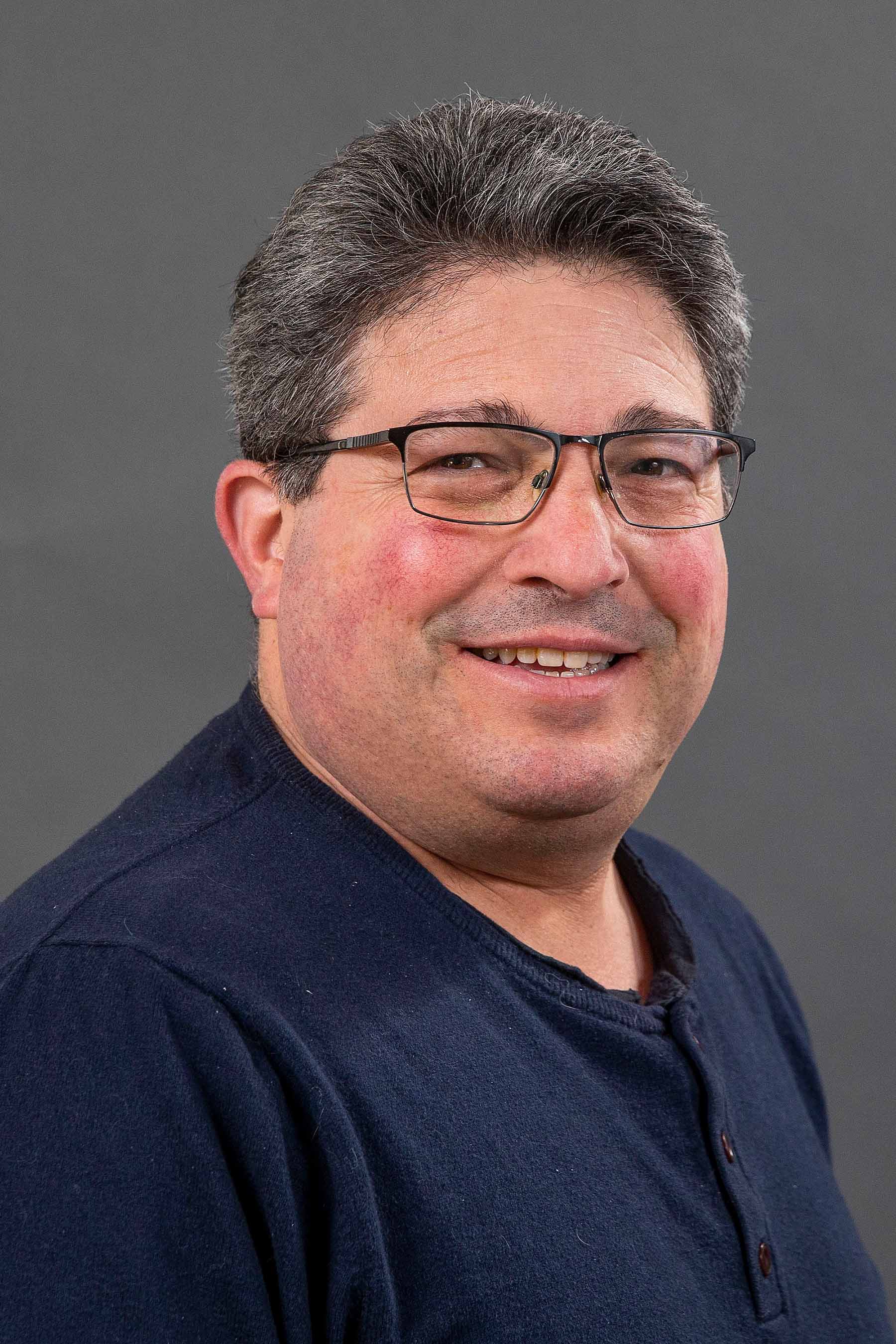 Marc Smith wearing a navy blue shirt against a gray background.