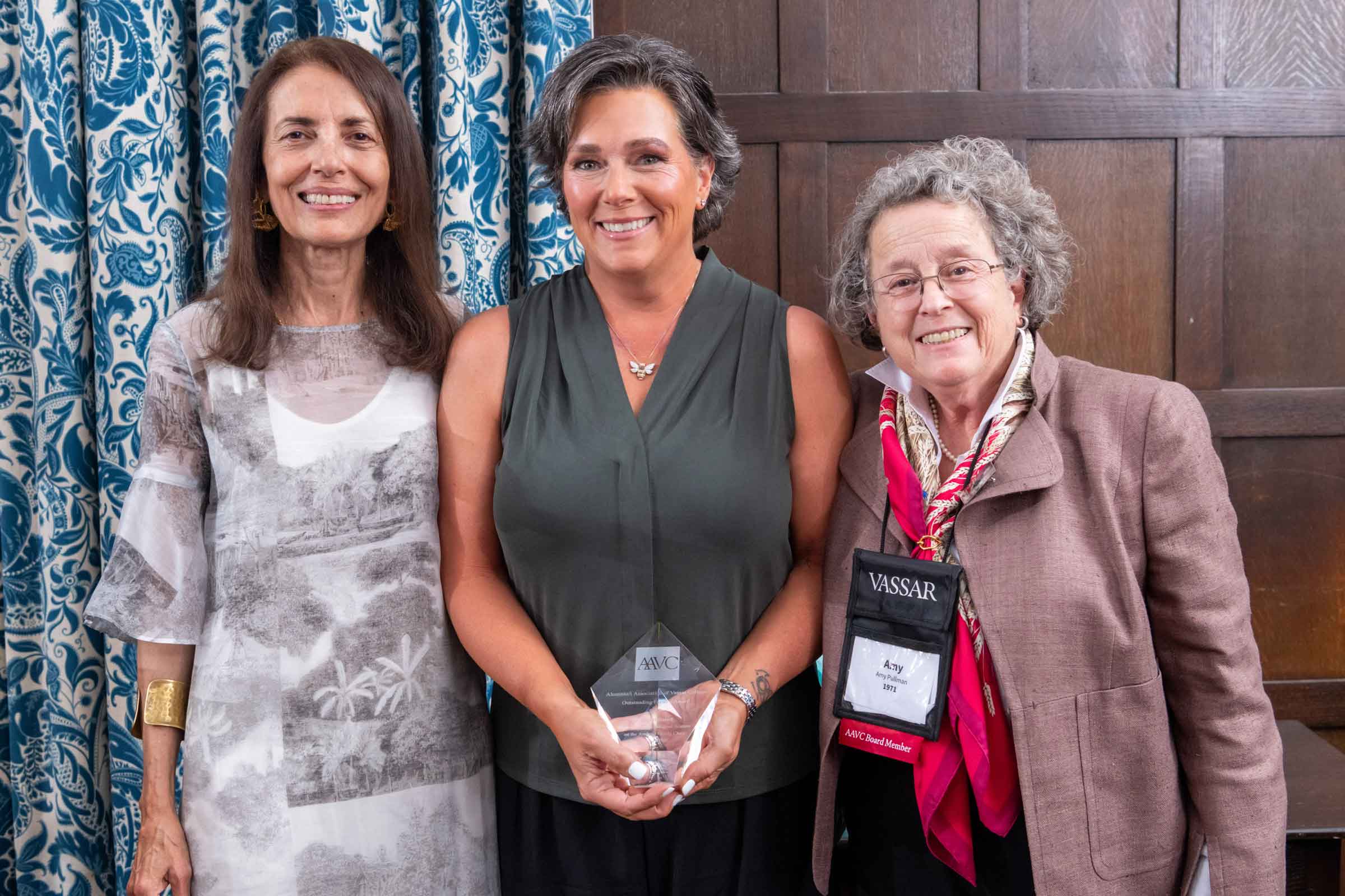 Three standing side by side smiling. The person in the center is holding an award.