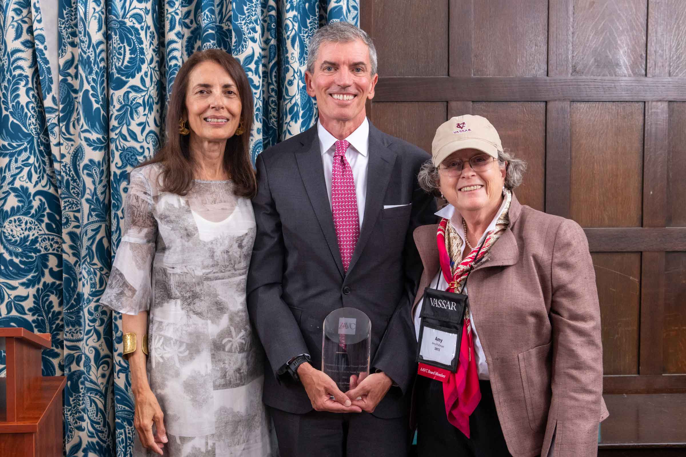 Three smiling people standing side by side. The person in the middle is holding an award