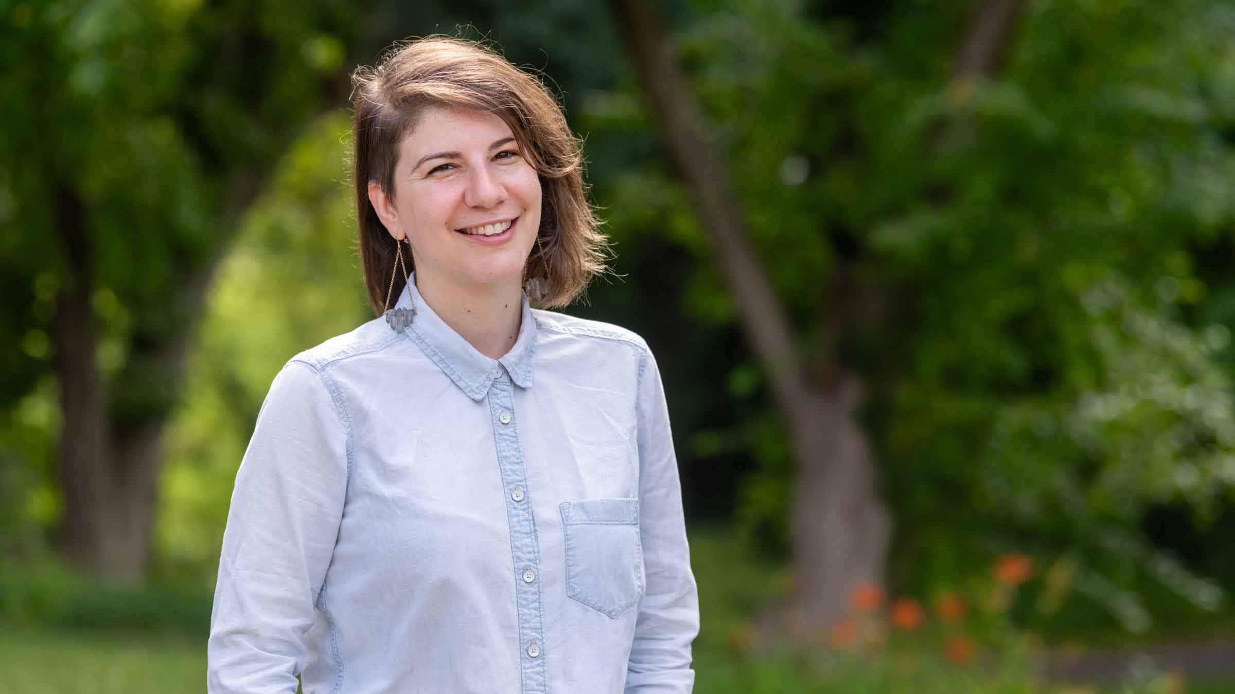 person standing and smiling for the camera in front of green foliage