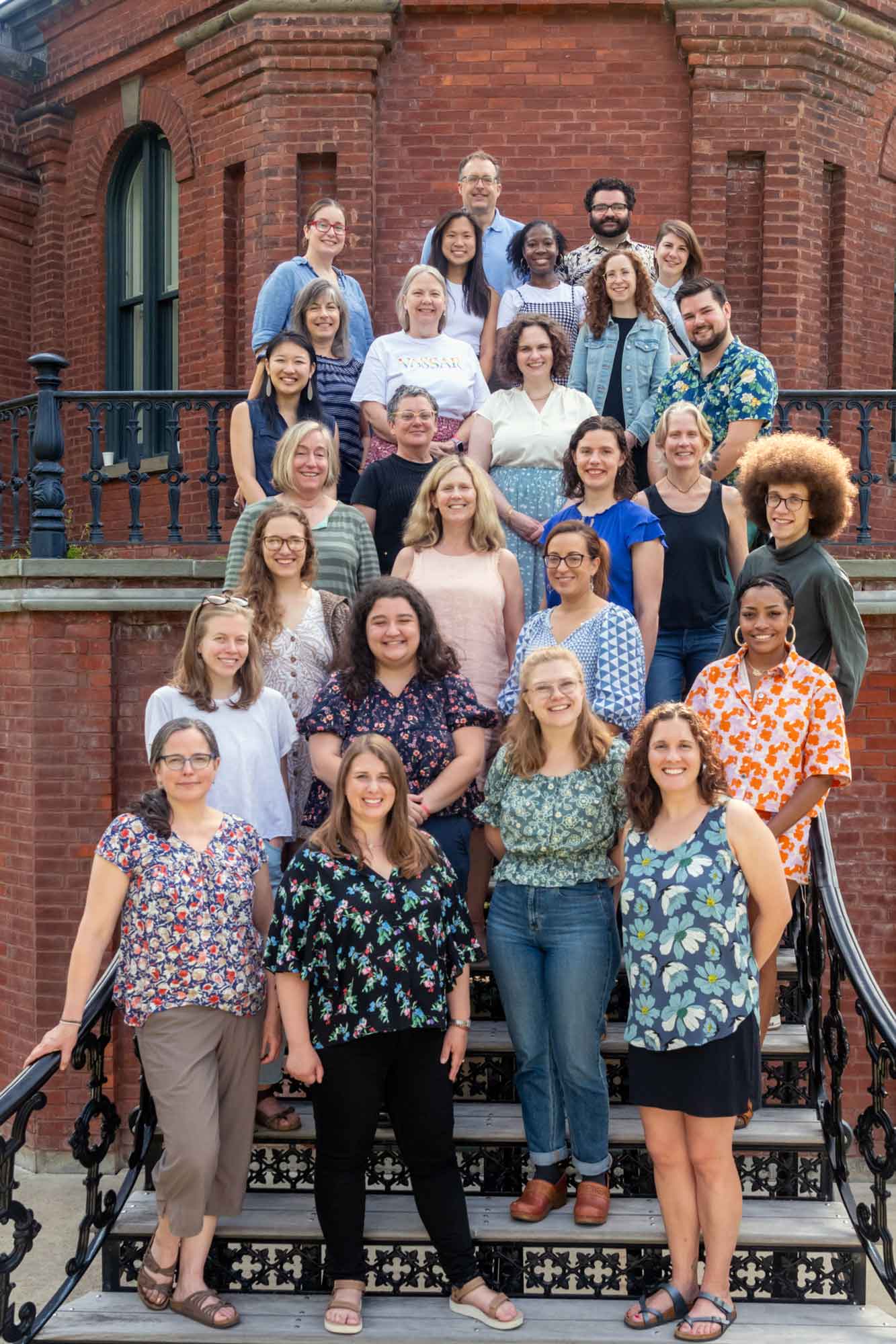 A group of people gathered on the steps of a brick building smiling for the camera