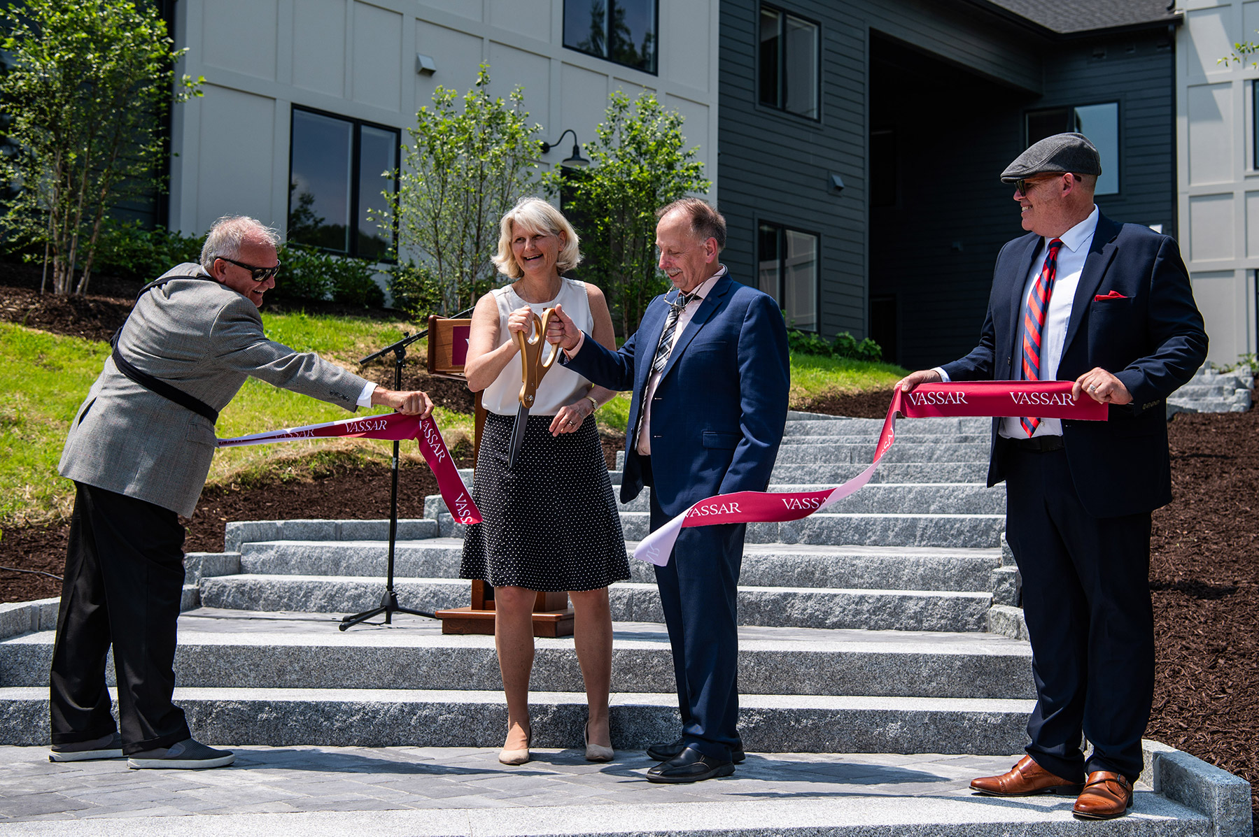 Man and woman holding giant scissors cutting a red ribbon with "Vassar" printed on the ribbon.