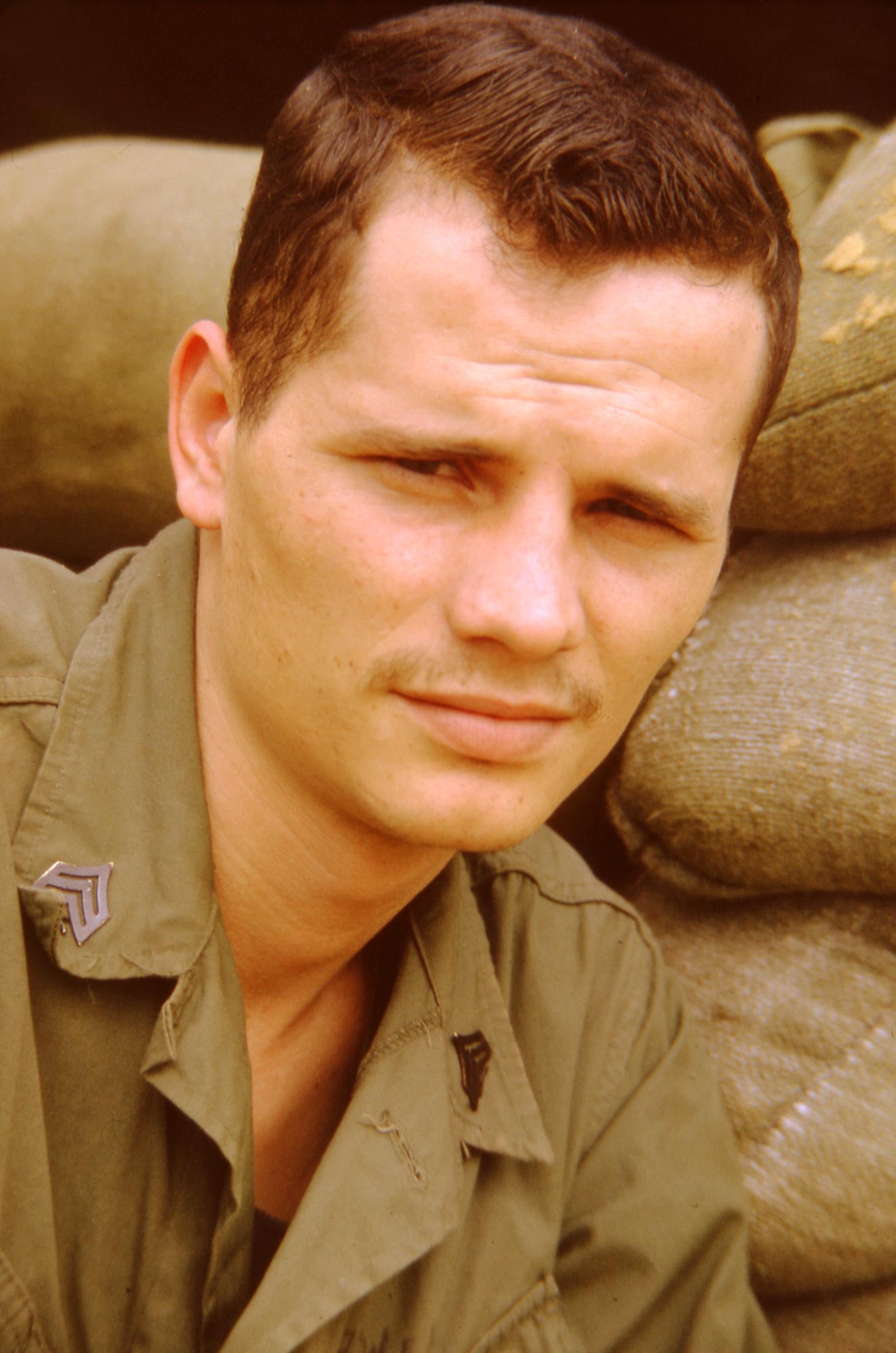 Headshot of a soldier in army fatigues with a mustache and a serious look facial expression