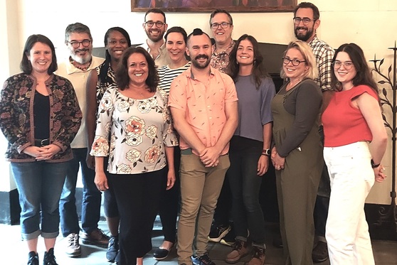 Large group of professors standing for a picture in a classroom.