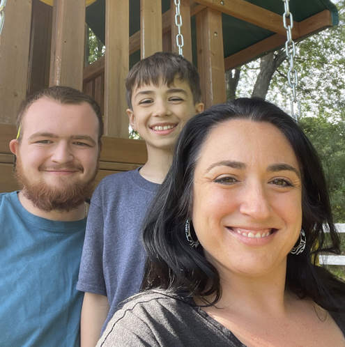 A photo of three people smiling at the camera. The leftmost person has short brown hair, a beard and mustache, and a blue shirt. The middle person has short brown hair. The rightmost person has long black hair and a gray shirt.