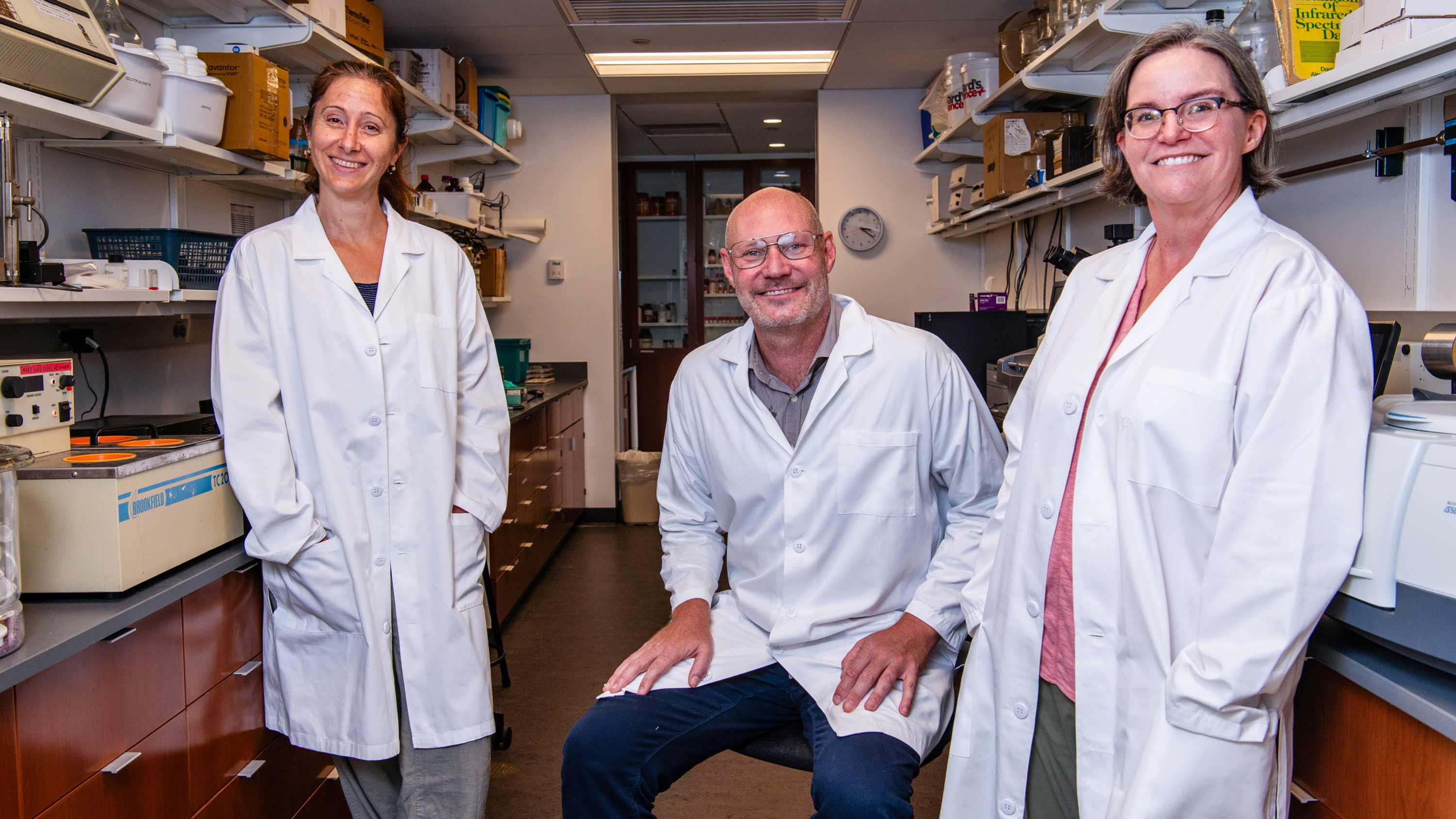 Three people standing in a science laboratory with white labcoats on.