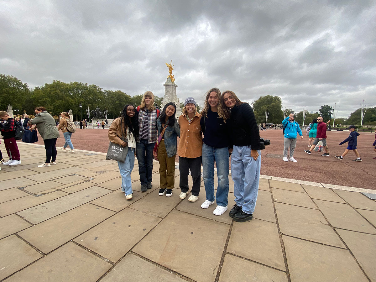 Group of people standing in front of the Victoria Memorial in London, a white statue with gold detail.