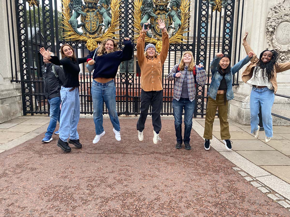 Group of people jumping in front of a large iron, decorative gate