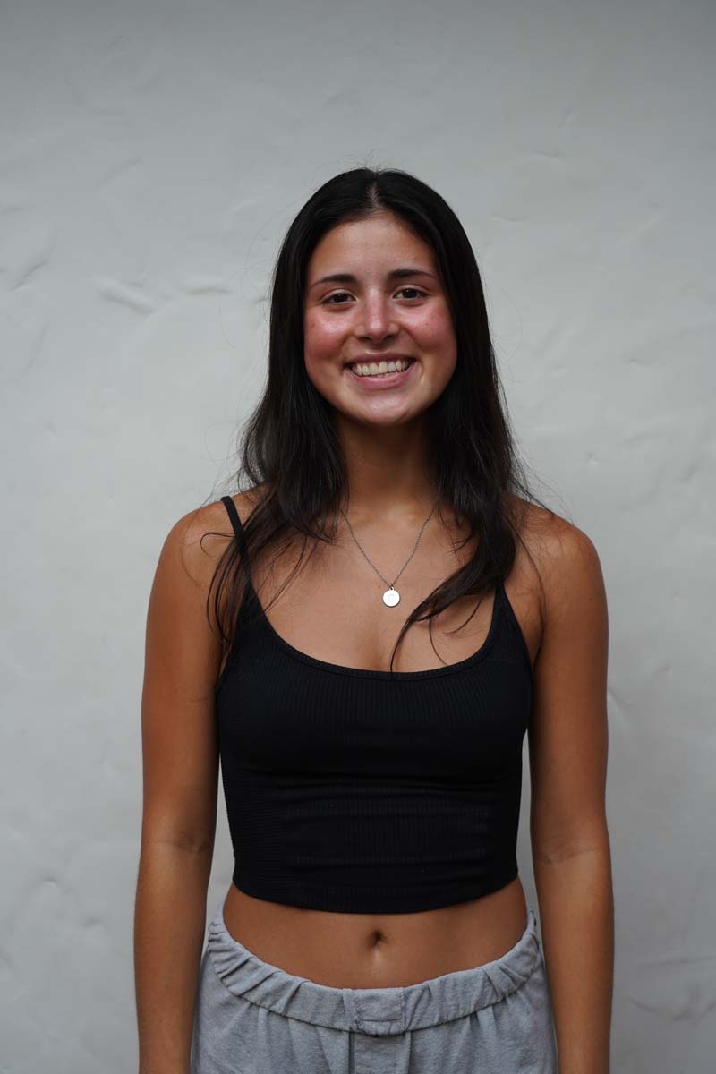 A person with long dark brown hair and a black tank top smiles at the viewer.