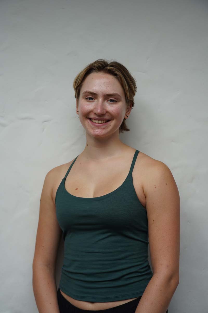 A person with long light brown hair and a dark green tank top smiles at the viewer.