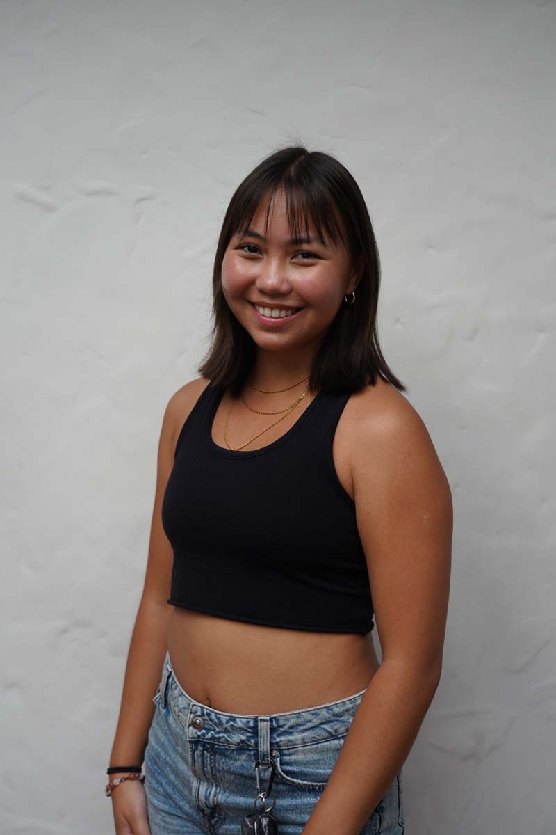 A person with long black hair and a black tank top smiles at the viewer.