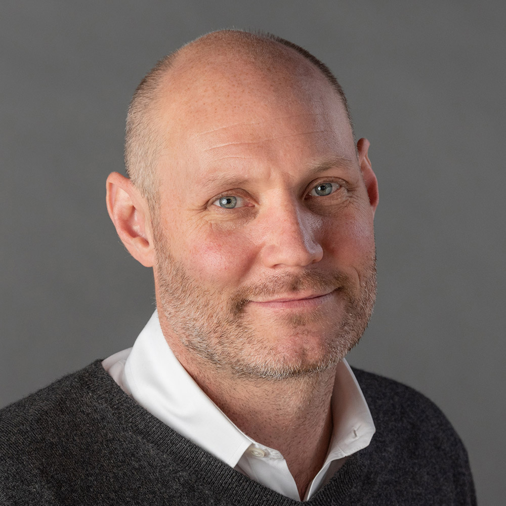 Bald person smiling in front of a grey backdrop.