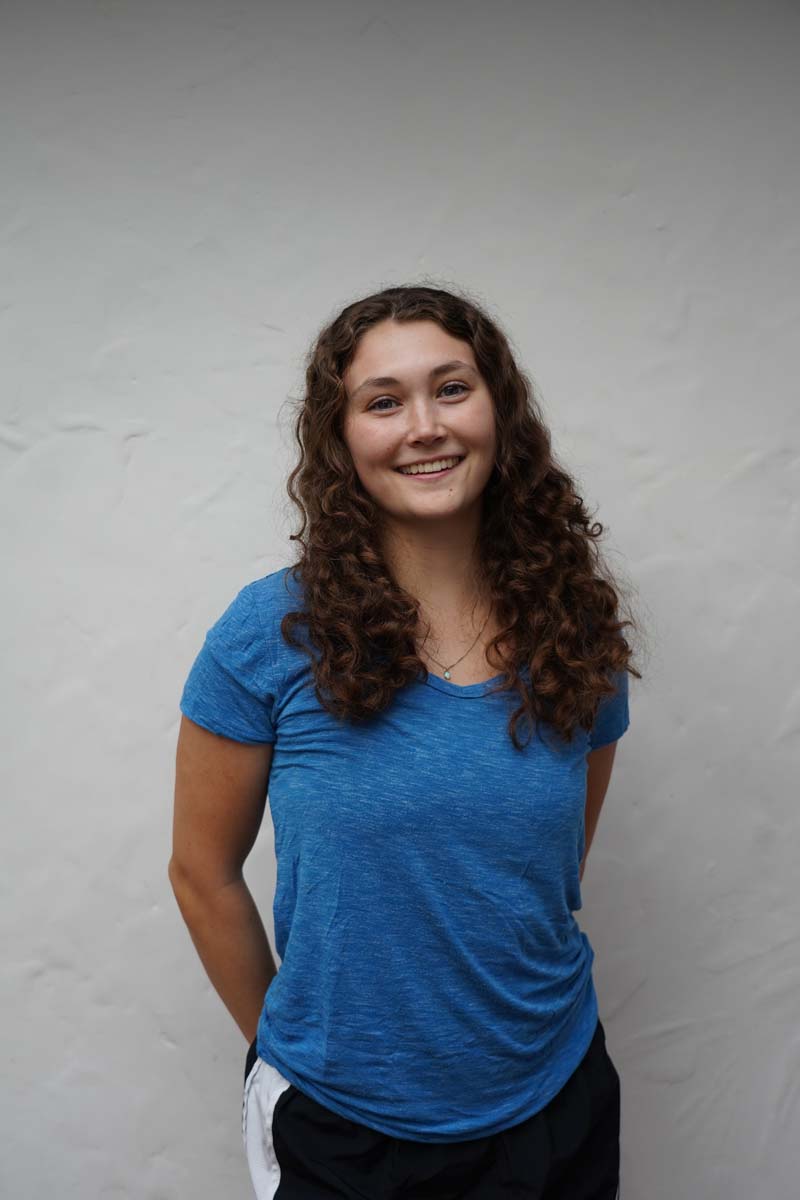 A person with long brown hair and a blue T shirt smiles at the viewer.