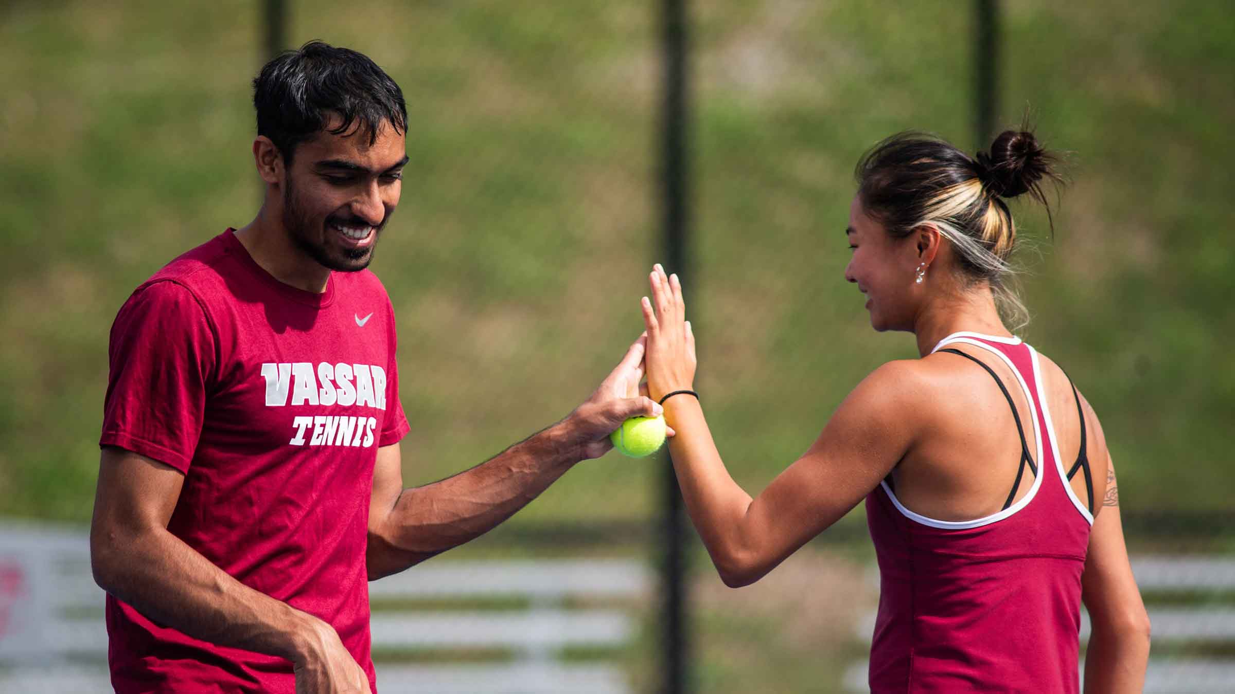 two people in tennis gear, one holding a ball, giving each other a high five