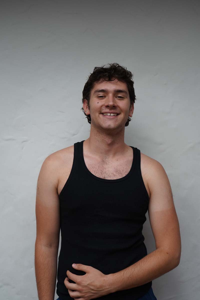 A person with short dark hair and a black tank top smiles at the viewer.