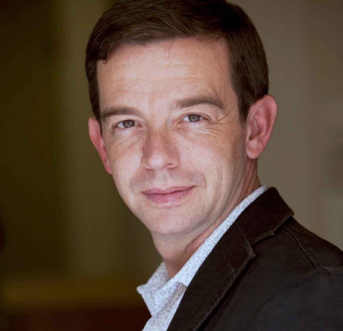 A headshot of a person with short reddish-brown hair and a black denim jacket looking at the viewer.