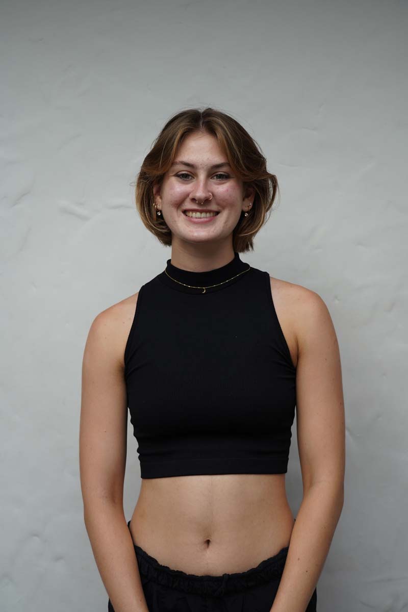 A person with mid-length brown hair and a black tank top smiles at the viewer.