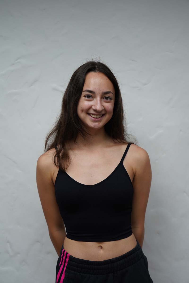 A person with long dark brown hair and a black tank top smiles at the viewer.