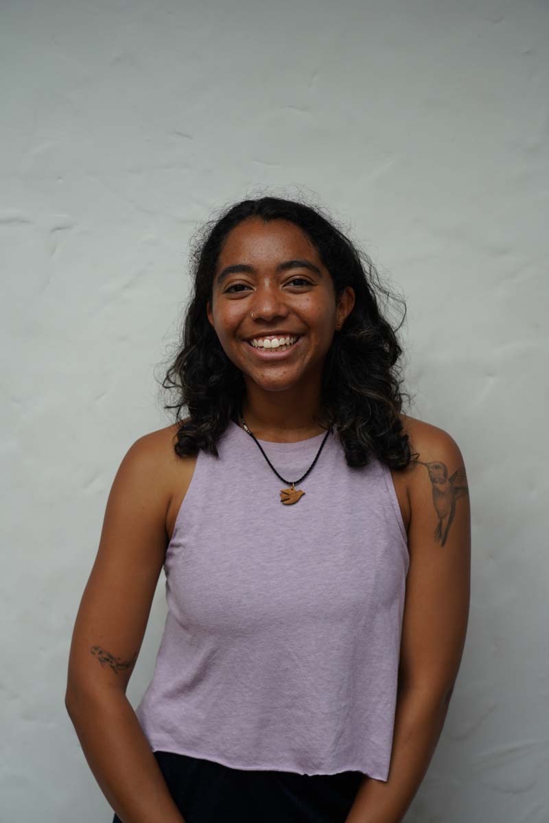 A person with long black hair and a lavender T-shirt smiles at the viewer.