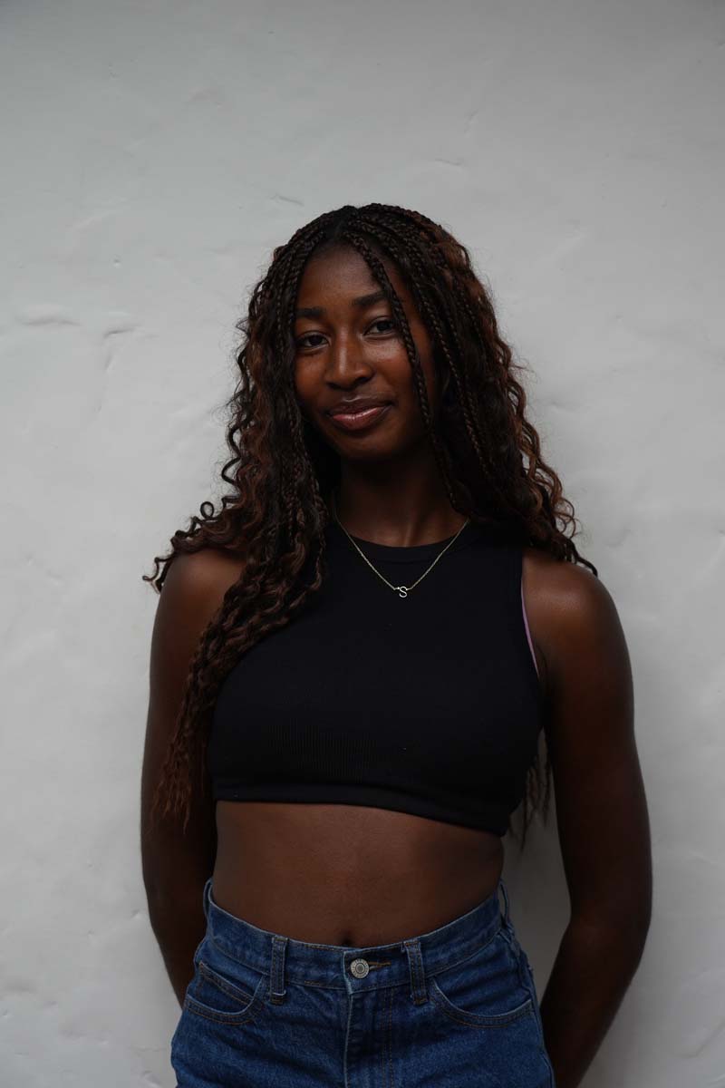 A person with long black curly hair and a black tank top smiles at the viewer.