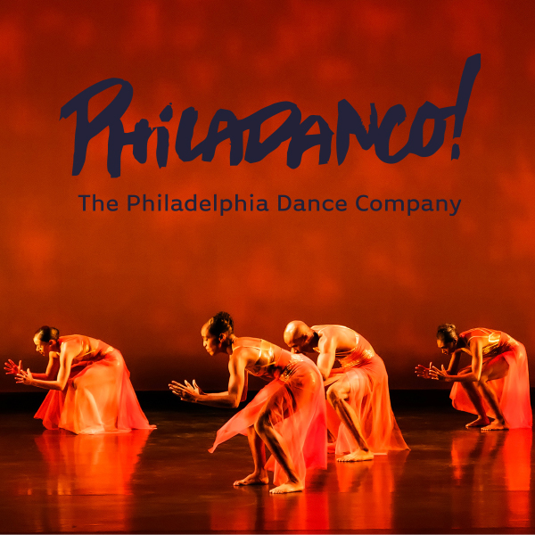 Four dancers on stage reach forward over partially bent knees with flowing orange gauzy skirts, bathed in a warm orange glow against a red backdrop.