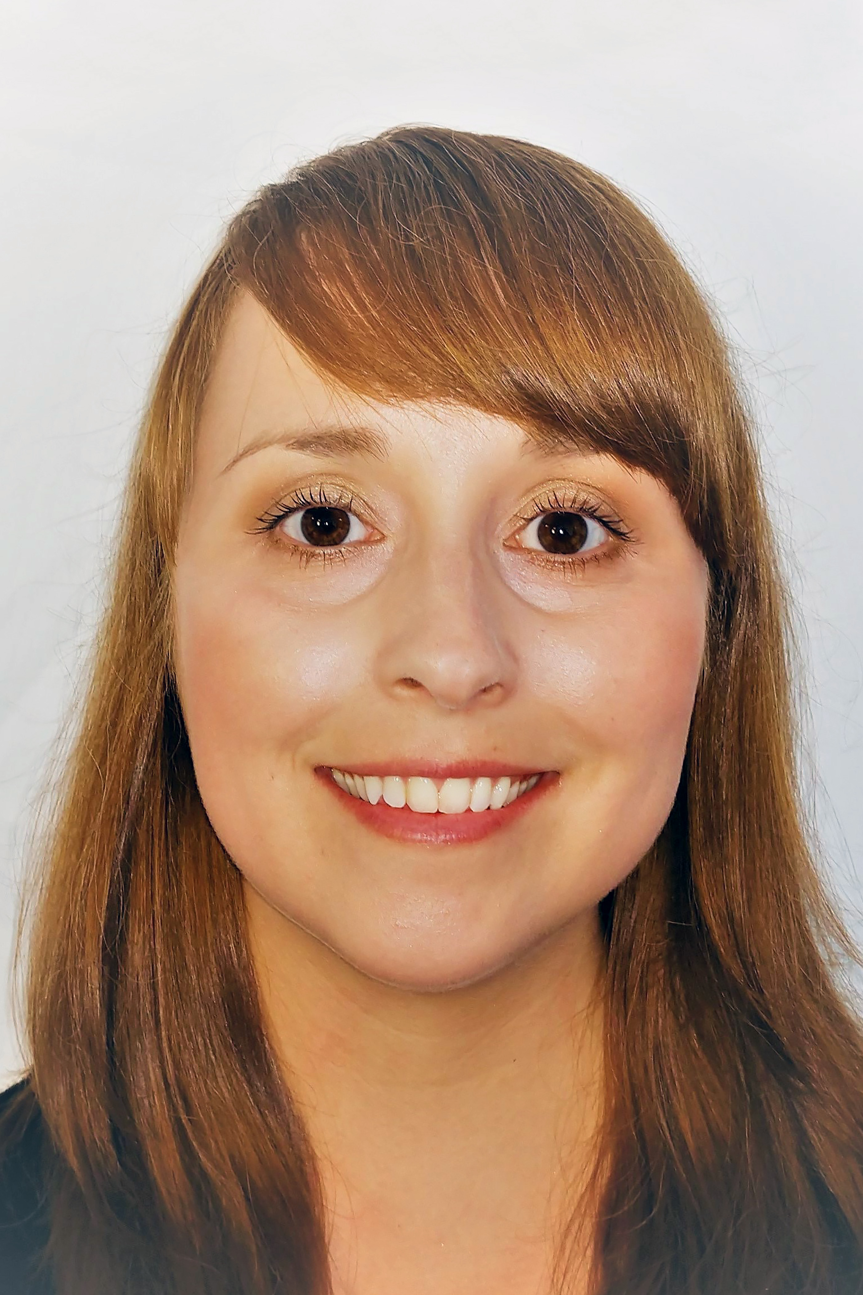 Woman with shoulder-length copper brown hair in front of a white backdrop smiling for the camera.