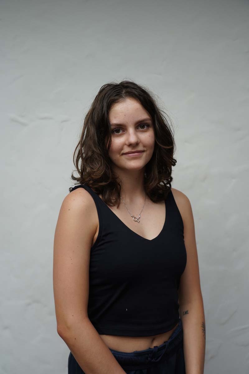 A person with long dark brown hair and a black tank top smiles at the viewer.