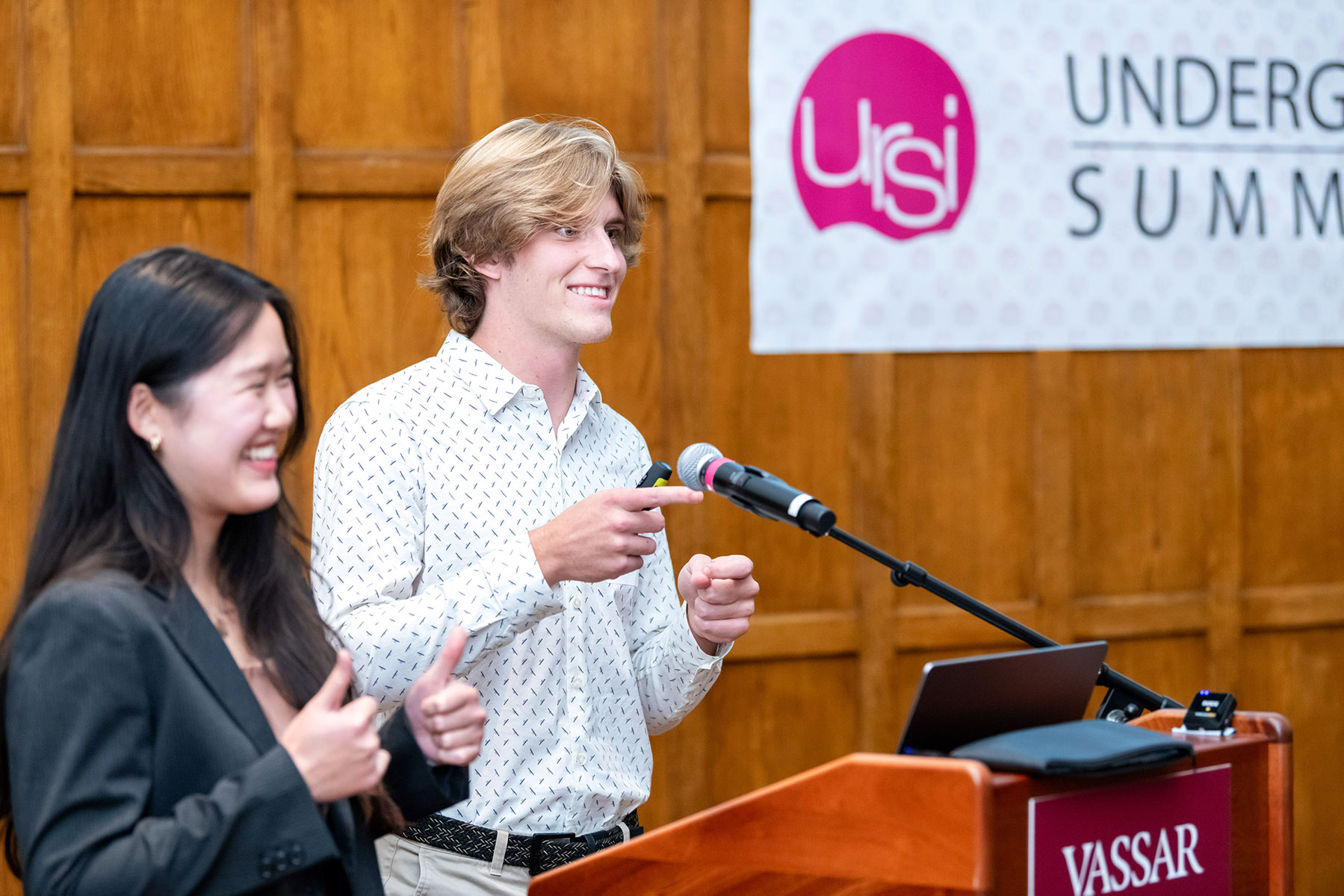 Two people standing at a podium on a stage with a banner in the background that reads, "URSI: Undergraduate Research Summer Institute."
