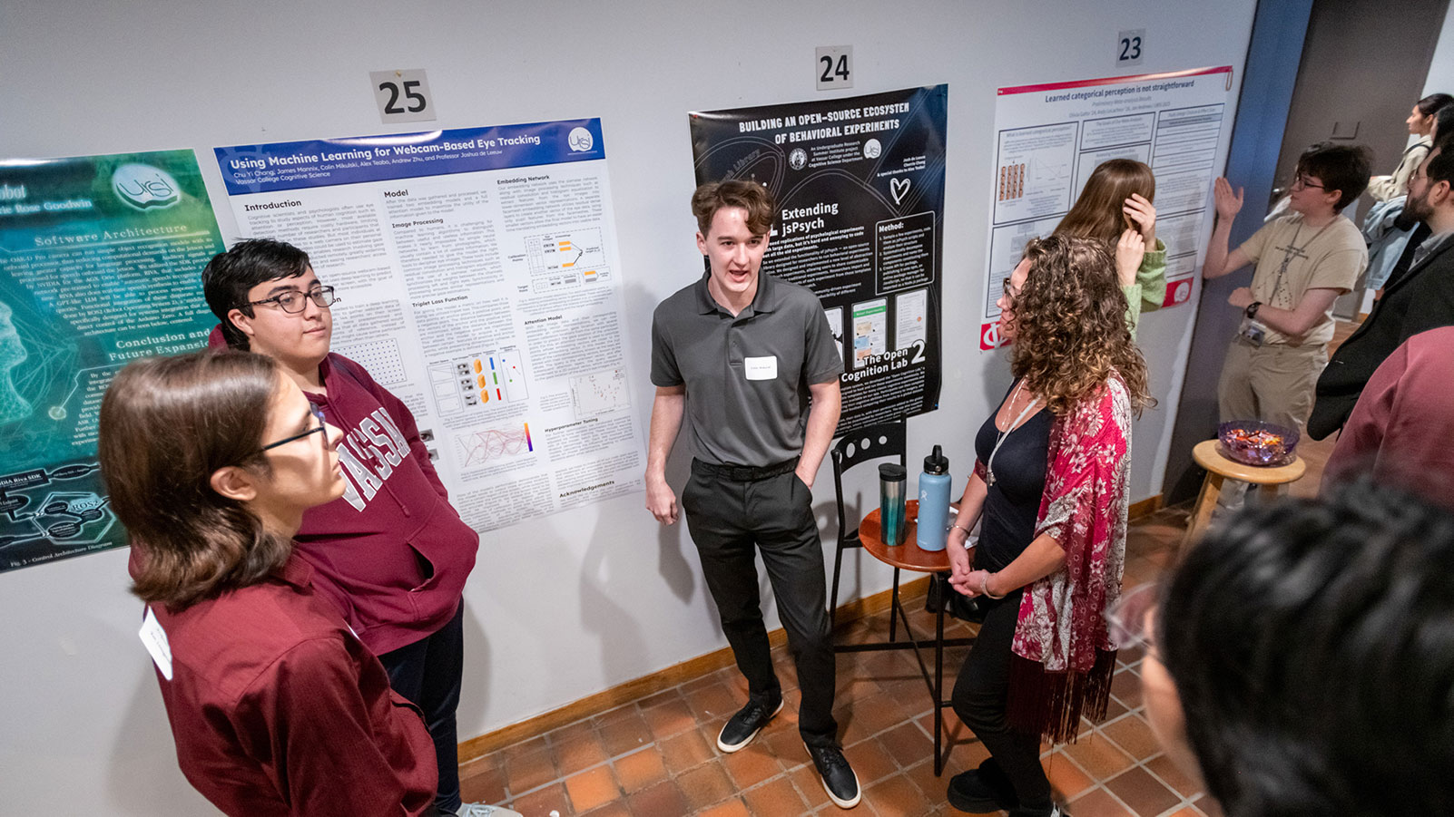 Groups of people standing in front of project posters on the wall while people listen.