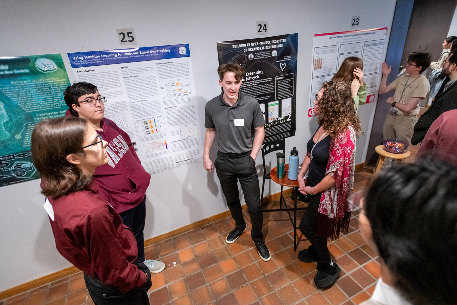 Groups of people standing in front of project posters on the wall while people listen.