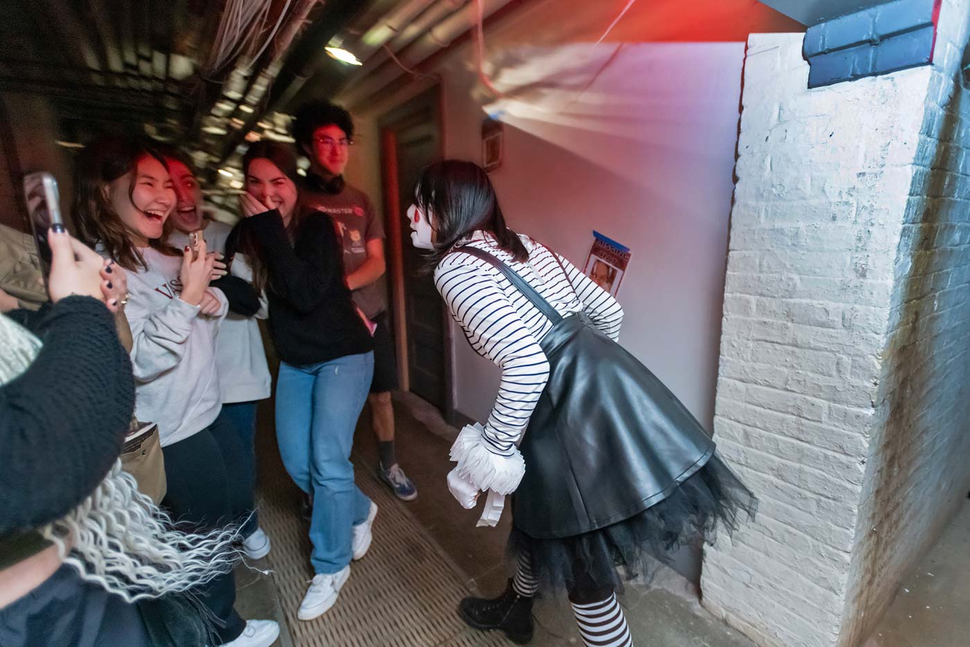 A person in a black dress and black-and-white-striped stockings and shirt frightens a group of people.
