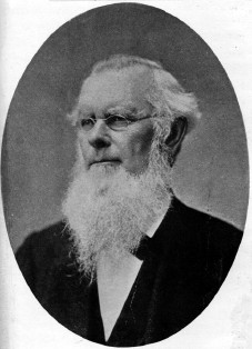 A black and white photo of Milo Jewett, a person with short white hair, an enormous white beard, and a black jacket.