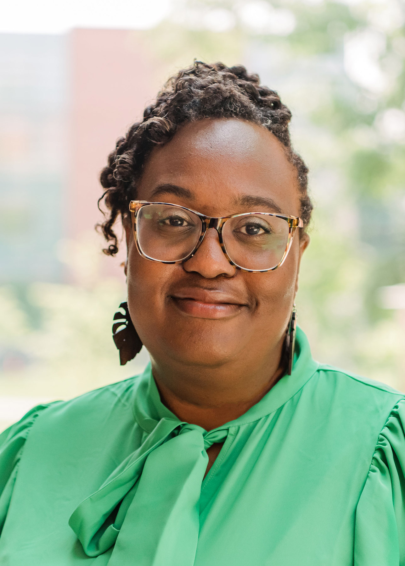 Person with glasses and a green shirt smiling for the camera.