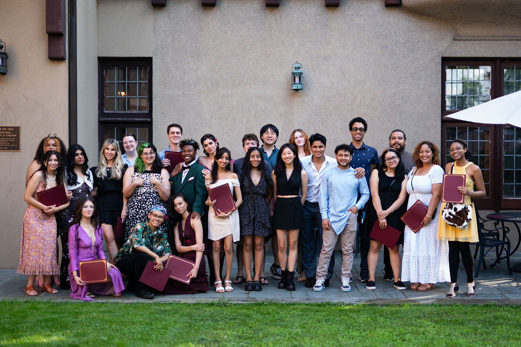 Large group of people standing outside in front of a wall with grass in front of them. They are all smiling with some of them holding awards.