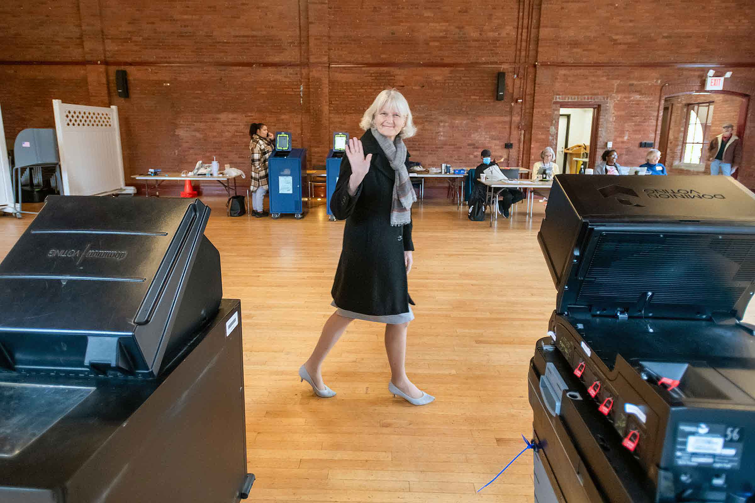 A person walking and waving to the camera at a polling site.