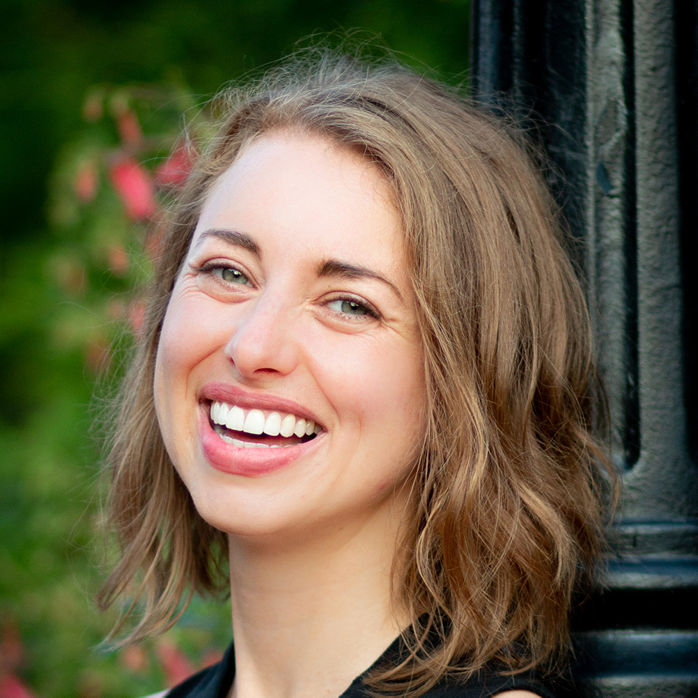 A person with long light brown hair smiles at the viewer.